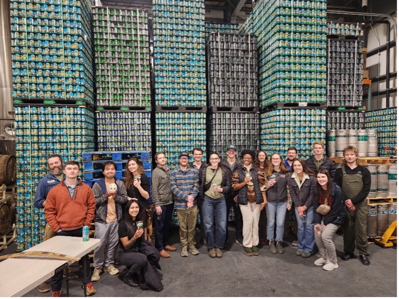 Group celebration in a brewery surrounded by colorful beverage cans in a lively warehouse.