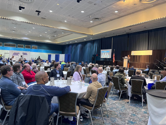 Professional conference session with engaged attendees and a speaker delivering a presentation.