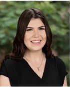 Smiling young woman in a casual black top with a natural outdoor backdrop.