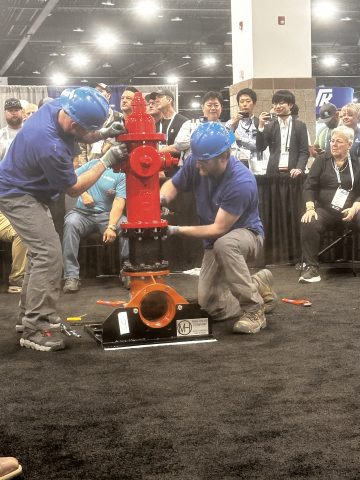 Technicians demonstrate fire hydrant assembly at a trade show, showcasing fire safety innovations.